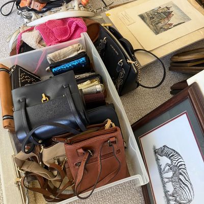 Sale Photo Thumbnail #24: Collection of women's handbags and small leather goods stored in a clear plastic bin alongside framed zebra artwork and matted architectural prints.