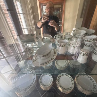 Sale Photo Thumbnail #150: Collection of fine china dining pieces with a festive holly leaf border, displayed inside a glass hutch.