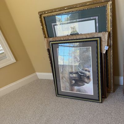 Sale Photo Thumbnail #29: Collection of framed artwork leaning against a wall, featuring an elephant print in a dark wood frame alongside large gilt-framed pieces.