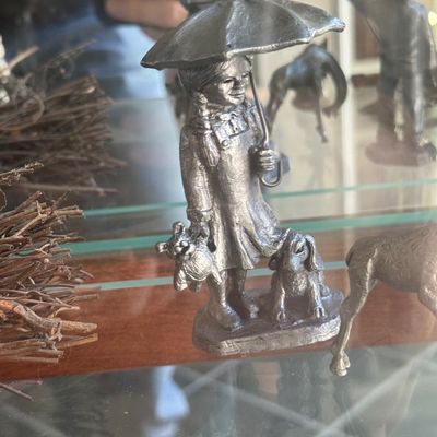 Sale Photo Thumbnail #144: Pewter miniature figurine depicting a young girl holding an umbrella, accompanied by a small dog and holding a doll.