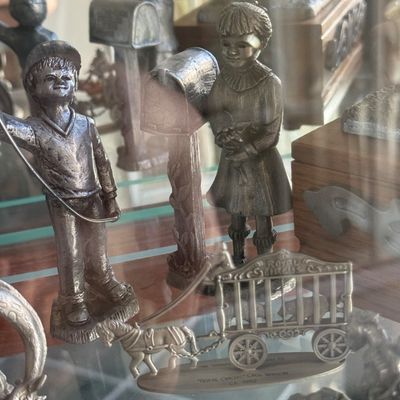 Sale Photo Thumbnail #147: Collection of vintage pewter metal figurines displayed in a glass cabinet, including children by a mailbox and a miniature Royal Circus cage wagon.