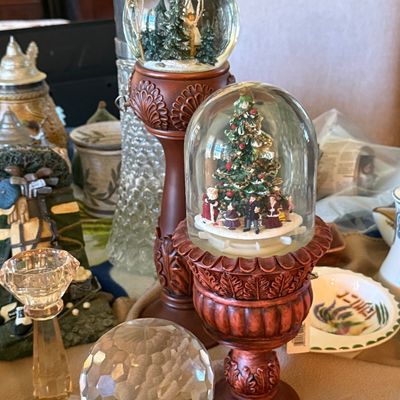 Sale Photo Thumbnail #49: Two resin Christmas snow globes on ornate pedestal bases, featuring winter tree scenes and holiday figurines.