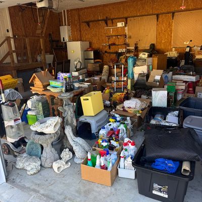 Sale Photo Thumbnail #19: Garage packed with estate sale items, including concrete garden statues, cleaning supplies, pet carriers, luggage, and storage totes.