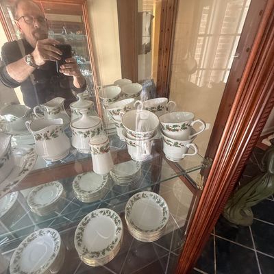Sale Photo Thumbnail #151: Collection of holiday-themed porcelain tableware featuring a holly pattern, arranged inside a glass display cabinet. Includes teacups, saucers, creamers, and covered sugar bowls.