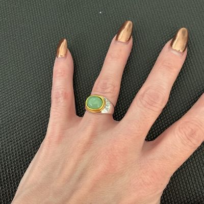 Sale Photo Thumbnail #210: A stylish ring featuring a smooth, oval-shaped light green stone cabochon set in a gold-tone bezel over a textured silver-tone band. Ring mandrel photos show a size of approximately 6. Light surface wear consistent with previous use.