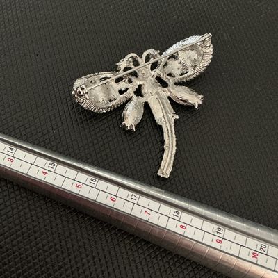 Sale Photo Thumbnail #198: A silver-tone dragonfly brooch featuring sparkling light green, blue, and yellow rhinestone accents in various cuts. Includes a standard pin-back clasp mechanism on the reverse. Appears to be in very good condition with all stones intact.
