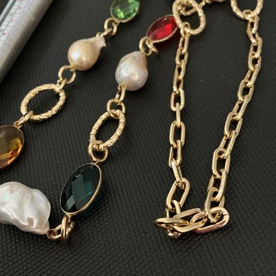 Sale Photo Thumbnail #139: Gold-tone chain station necklace featuring large, irregularly shaped baroque pearls interspersed with faceted oval crystals in red, green, amber, and dark green. The necklace combines a paperclip link chain with textured circular accent links. Good pre-ow