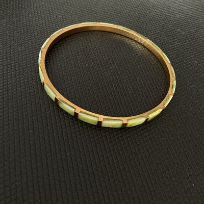 Sale Photo Thumbnail #177: A slim, brass-tone bangle bracelet featuring channel-set rectangular light green segments around the outer band. The item shows light wear consistent with age, including mild tarnish/patina on the metal frame.