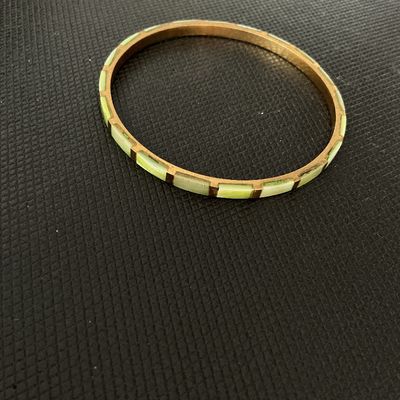 Sale Photo Thumbnail #176: A slim, brass-tone bangle bracelet featuring channel-set rectangular light green segments around the outer band. The item shows light wear consistent with age, including mild tarnish/patina on the metal frame.