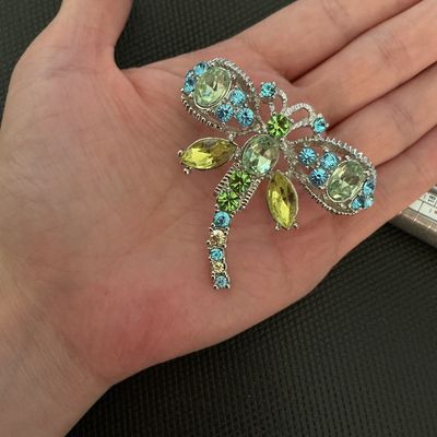 Sale Photo Thumbnail #200: A silver-tone dragonfly brooch featuring sparkling light green, blue, and yellow rhinestone accents in various cuts. Includes a standard pin-back clasp mechanism on the reverse. Appears to be in very good condition with all stones intact.