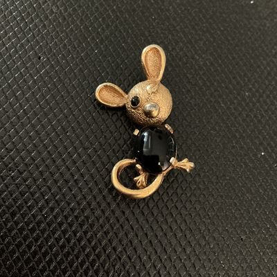 Sale Photo Thumbnail #223: Charming vintage gold-tone mouse brooch featuring a textured head, black cabochon stone body, small black eye detail, and a curved tail. C-clasp fastener on the back shows minor verdigris/patina near the pin stem hinge, otherwise in good condition with li