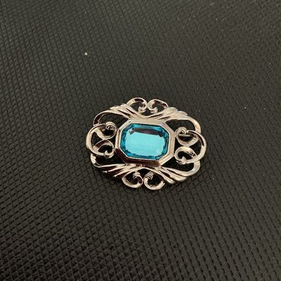 Sale Photo Thumbnail #231: Silver-tone metal brooch featuring an openwork scroll design surrounding a central emerald-cut aqua/light blue rhinestone or glass stone. Back shows a standard pin stem and rollover safety clasp. Good pre-owned condition with light wear.