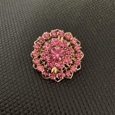Sale Photo Thumbnail #163: A vintage round starburst or rosette-style brooch featuring tiered pink faceted rhinestones set in a gold-tone filigree metal frame. The back features an openwork lattice pattern and a standard rollover safety clasp pin mechanism. Appears to be in good vi
