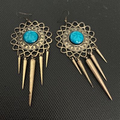 Sale Photo Thumbnail #216: A pair of statement dangle earrings featuring antique-tone brass metalwork, round teal blue central cabs with star/sunburst details, and hanging cone/spike charms. Fitted with French wire hooks for pierced ears. Good condition with minimal wear.