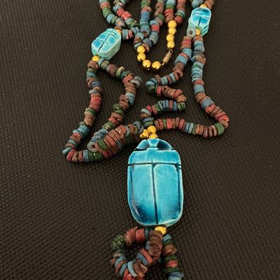 Sale Photo Thumbnail #149: Egyptian revival style multi-strand beaded necklace featuring a large bright blue ceramic or faience scarab beetle pendant, smaller scarab accent beads, and multicolored disc beads. Finished with gold-tone barrel clasp closure. Shows light signs of age-ap