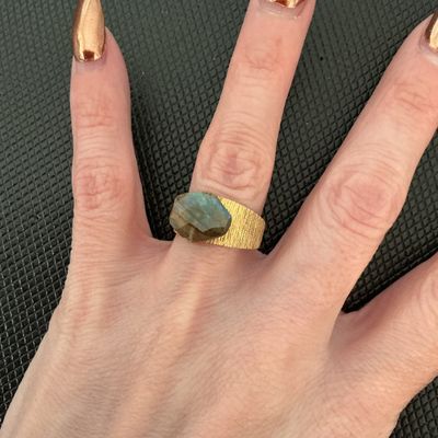 Sale Photo Thumbnail #183: Gold-tone wide band statement ring featuring a textured/brushed finish and a faceted labradorite center stone showing iridescent blue-green flashes. Size measures approximately 7 on a ring mandrel. Good condition with light signs of wear.