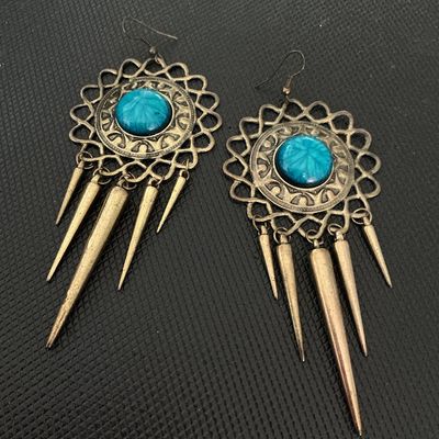 Sale Photo Thumbnail #215: A pair of statement dangle earrings featuring antique-tone brass metalwork, round teal blue central cabs with star/sunburst details, and hanging cone/spike charms. Fitted with French wire hooks for pierced ears. Good condition with minimal wear.