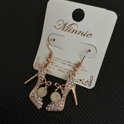 Sale Photo Thumbnail #135: Pair of gold-tone dangle earrings shaped like high heel pumps, encrusted with clear rhinestones and featuring a small bow detail with a faux pearl or round accent stone. Brand card marked 'Minnie'. Items are on original retail card backing and appear unus