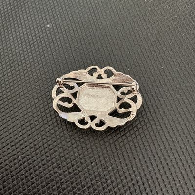 Sale Photo Thumbnail #232: Silver-tone metal brooch featuring an openwork scroll design surrounding a central emerald-cut aqua/light blue rhinestone or glass stone. Back shows a standard pin stem and rollover safety clasp. Good pre-owned condition with light wear.