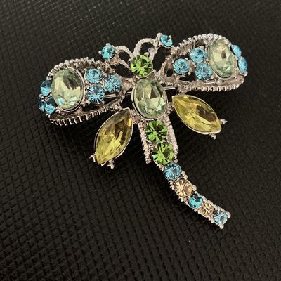 Sale Photo Thumbnail #196: A silver-tone dragonfly brooch featuring sparkling light green, blue, and yellow rhinestone accents in various cuts. Includes a standard pin-back clasp mechanism on the reverse. Appears to be in very good condition with all stones intact.