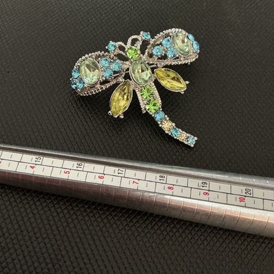 Sale Photo Thumbnail #197: A silver-tone dragonfly brooch featuring sparkling light green, blue, and yellow rhinestone accents in various cuts. Includes a standard pin-back clasp mechanism on the reverse. Appears to be in very good condition with all stones intact.