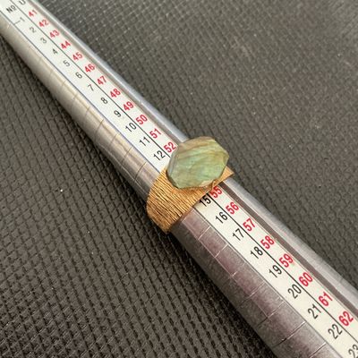 Sale Photo Thumbnail #184: Gold-tone wide band statement ring featuring a textured/brushed finish and a faceted labradorite center stone showing iridescent blue-green flashes. Size measures approximately 7 on a ring mandrel. Good condition with light signs of wear.