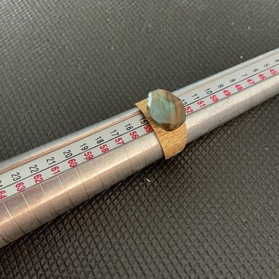Sale Photo Thumbnail #185: Gold-tone wide band statement ring featuring a textured/brushed finish and a faceted labradorite center stone showing iridescent blue-green flashes. Size measures approximately 7 on a ring mandrel. Good condition with light signs of wear.