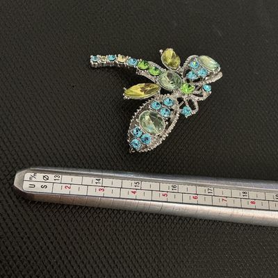 Sale Photo Thumbnail #199: A silver-tone dragonfly brooch featuring sparkling light green, blue, and yellow rhinestone accents in various cuts. Includes a standard pin-back clasp mechanism on the reverse. Appears to be in very good condition with all stones intact.