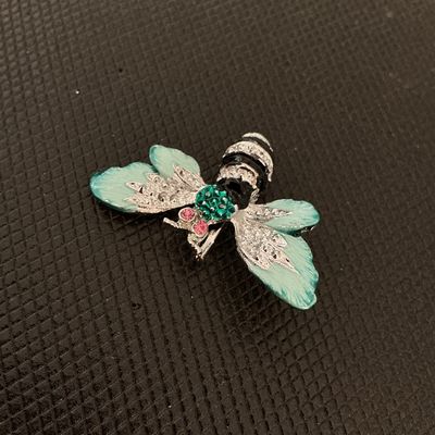 Sale Photo Thumbnail #218: A detailed bee brooch featuring silver-tone metal construction, light green enamel wing details, green rhinestones on the head, and pink rhinestone eyes. Black enamel striping decorates the body. Includes a standard pin back clasp mechanism. Appears in go