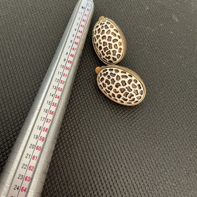 Sale Photo Thumbnail #222: Pair of vintage oval-shaped clip-on earrings featuring a cream and dark brown leopard/cheetah animal print pattern in enamel or resin with a antique brass-tone metal backing and clip hardware. Shows light age-appropriate wear and patina on the metal hardw