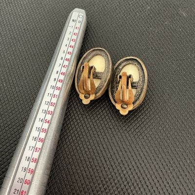 Sale Photo Thumbnail #221: Pair of vintage oval-shaped clip-on earrings featuring a cream and dark brown leopard/cheetah animal print pattern in enamel or resin with a antique brass-tone metal backing and clip hardware. Shows light age-appropriate wear and patina on the metal hardw
