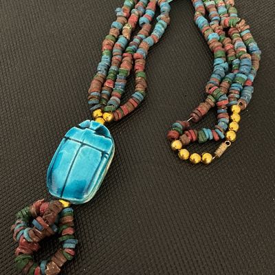 Sale Photo Thumbnail #150: Egyptian revival style multi-strand beaded necklace featuring a large bright blue ceramic or faience scarab beetle pendant, smaller scarab accent beads, and multicolored disc beads. Finished with gold-tone barrel clasp closure. Shows light signs of age-ap