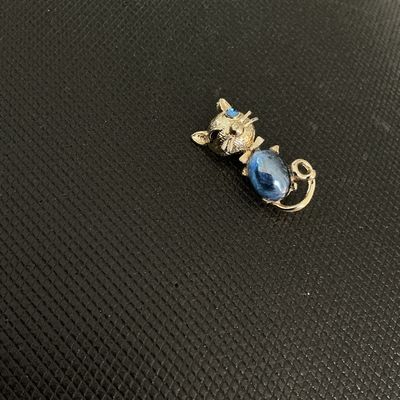 Sale Photo Thumbnail #201: A charming vintage gold-tone cat brooch featuring a textured finish, a bright blue cabochon body, and a blue rhinestone eye. Measures approximately 1.5 inches in length. In good vintage condition with minor wear consistent with age. Pin back fastener is f