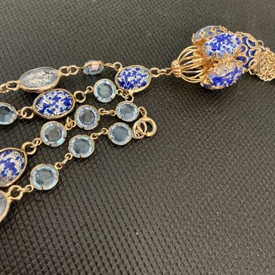 Sale Photo Thumbnail #153: Ornate vintage costume necklace featuring blue and silver foil art glass beads, light blue bezel-set crystals, and a detailed cage-style pendant with hanging chain tassel. Gold-tone chain settings with spring ring clasp closure. Excellent vintage conditio