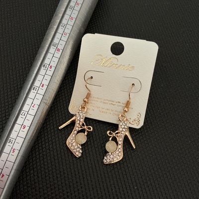 Sale Photo Thumbnail #136: Pair of gold-tone dangle earrings shaped like high heel pumps, encrusted with clear rhinestones and featuring a small bow detail with a faux pearl or round accent stone. Brand card marked 'Minnie'. Items are on original retail card backing and appear unus