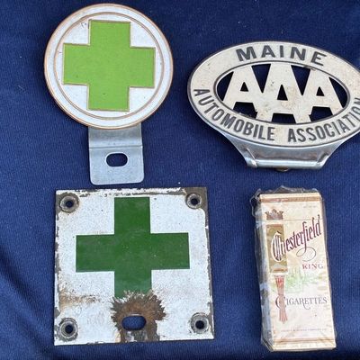 Sale Photo Thumbnail #36: Collection of vintage automotive collectibles including a Maine Automobile Association AAA emblem, green cross insignia badges, and a sealed pack of Chesterfield King cigarettes.