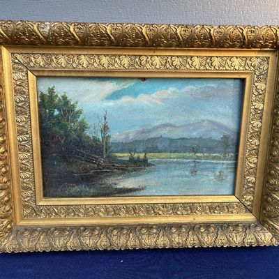 Sale Photo Thumbnail #34: Antique 19th-century oil landscape painting depicting a serene river and distant mountains, housed in an ornate gilded gesso frame.