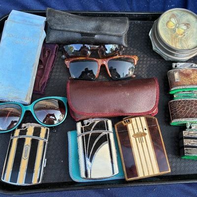 Collection of vintage accessories on a tray, including Art Deco enamel cigarette lighters, sunglasses, leather eyewear cases, a Dolce...