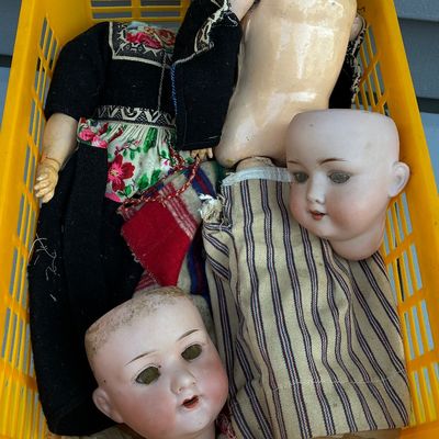 Sale Photo Thumbnail #67: Yellow plastic basket filled with vintage doll parts, including antique bisque doll heads and fabric-clad composite bodies.
