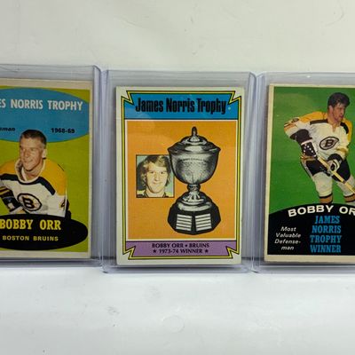 Sale Photo Thumbnail #86: Trio of vintage Topps Bobby Orr hockey trading cards, including James Norris Trophy subset cards from the late 1960s to 1970s, displayed in protective plastic top loaders.