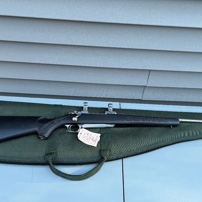 Sale Photo Thumbnail #60: Bolt-action rifle featuring a black synthetic stock and stainless steel barrel, resting on a green soft rifle case.