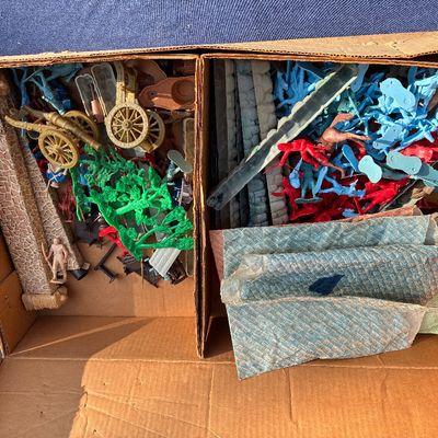 Sale Photo Thumbnail #8: Cardboard box filled with vintage plastic toy soldiers, cannons, foliage, and play set structures, likely Marx or similar mid-century brand.