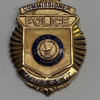 Sale Photo Thumbnail #41: Gold-tone Police Commissioner badge from Hooksett, New Hampshire, featuring blue enamel lettering and a central state seal.
