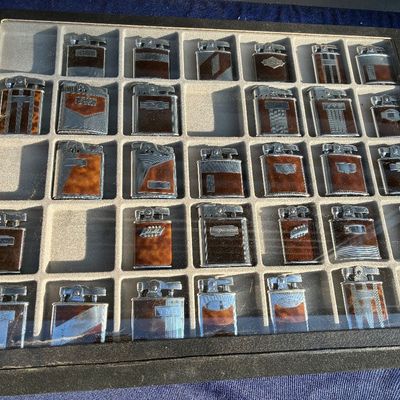 Collection of vintage Art Deco style pocket lighters displayed in a black framed shadowbox case with a divided felt tray.