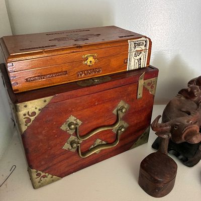 Sale Photo Thumbnail #39: Vintage Gran Cienfuegos wooden cigar box resting atop an Asian-style brass-bound wooden chest, alongside a carved wooden water buffalo figurine.