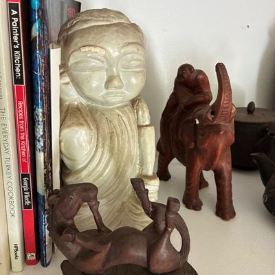 Sale Photo Thumbnail #37: Collection of carved decorative figurines, including a reclined Buddha bookend, a wooden elephant rider, and a carved horse lying on its back.
