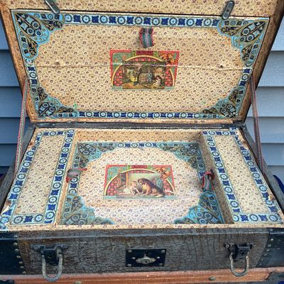 Sale Photo Thumbnail #35: Antique 19th-century steamer trunk featuring ornate floral wallpaper lining, decorative corner motifs, and lithograph prints inside the lid and tray.