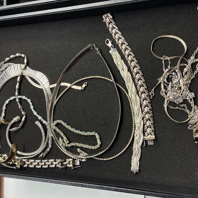 Sale Photo Thumbnail #122: Collection of sterling silver and silver-tone jewelry arranged in a black display tray, including chain necklaces, herringbone chokers, bracelets, and a cuff.