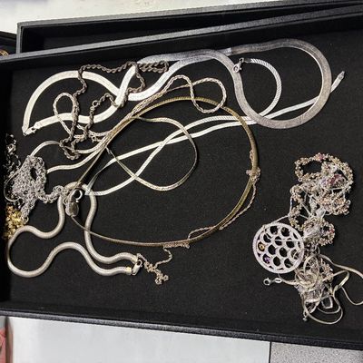 Sale Photo Thumbnail #121: Collection of sterling silver and gold-tone chain necklaces, including herringbone, omega, rope, and pendant designs, displayed in a black jewelry tray.