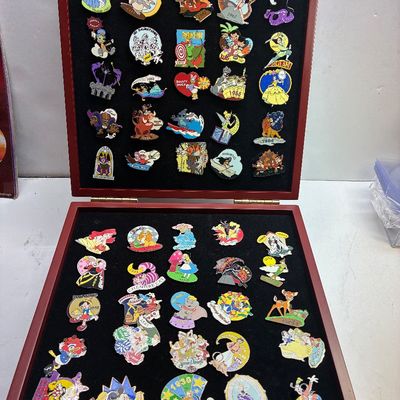 Sale Photo Thumbnail #109: Collection of Disney anniversary enamel trading pins displayed inside a two-tier wooden presentation case with a black felt lining.